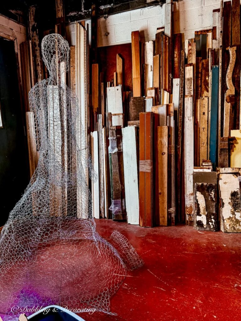 Wired mannequin figure in architectural salvaged room filled with old wood and doors.