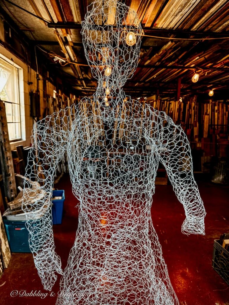 Wired mannequin figure in architectural salvaged room filled with old wood and doors.