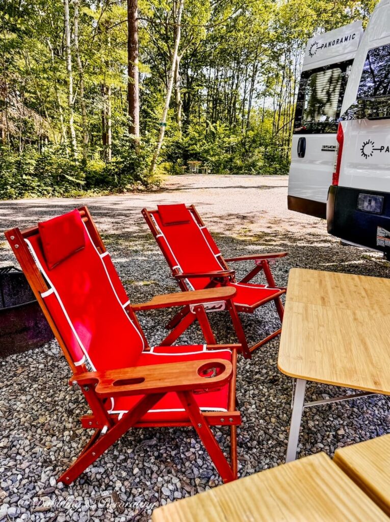 Two outdoor red teak chairs at campground in Maine with table and RV.