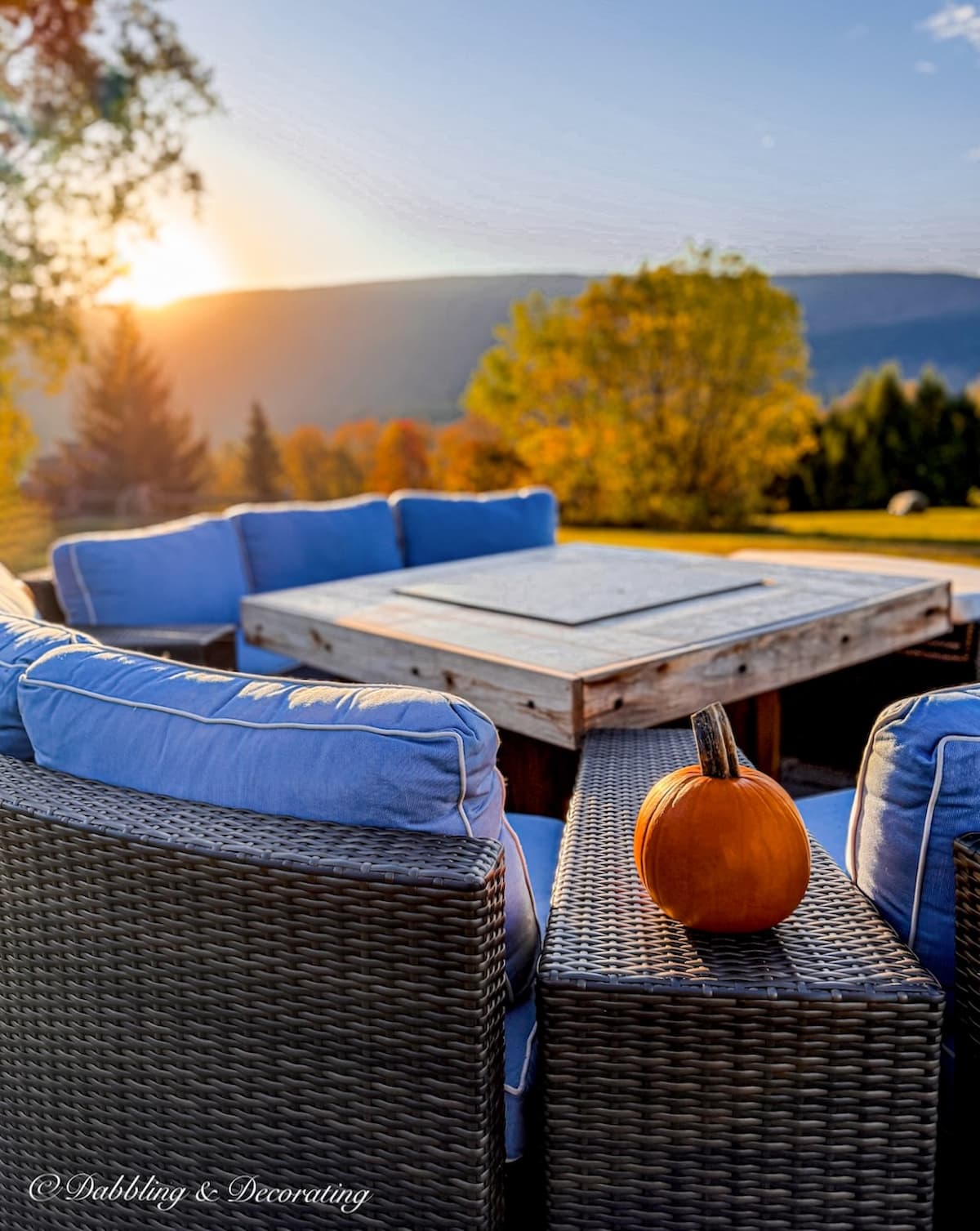 Fire pit with conversational set with blue cushions, pumpkin in the fall foliage mountains.