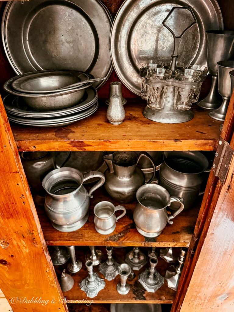 Antique pewter collection displayed in antique hutch with height and balance.