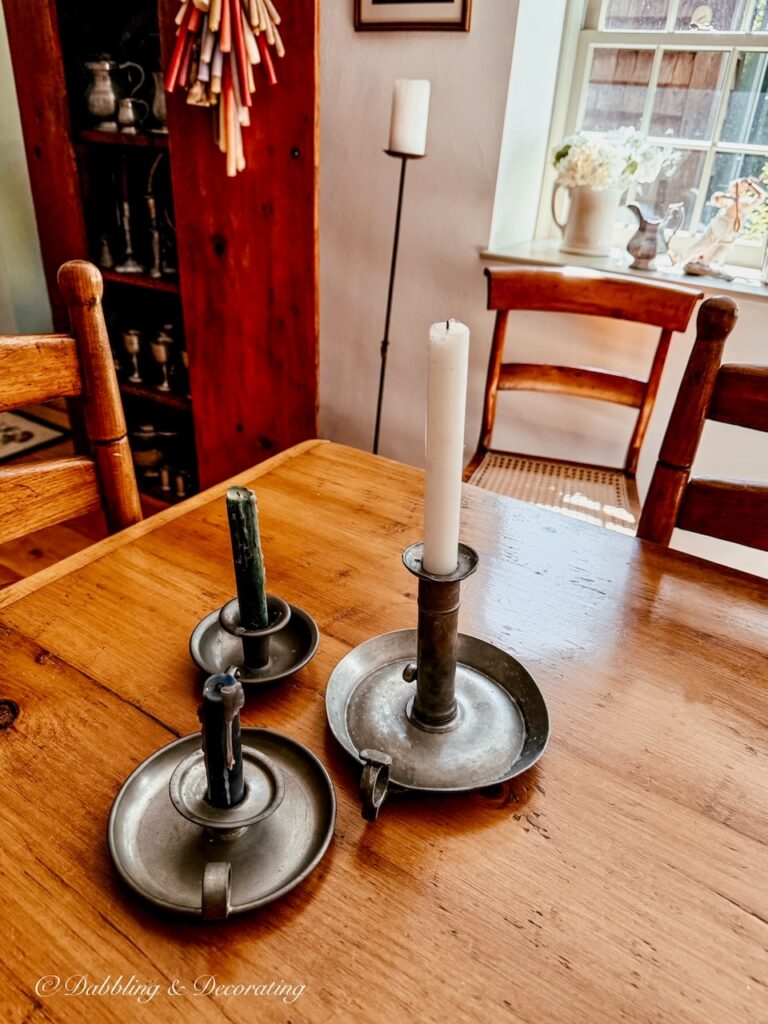 Pewter candlesticks at the end of a vintage table in dining room looking onto antique hutch styled with pewter.