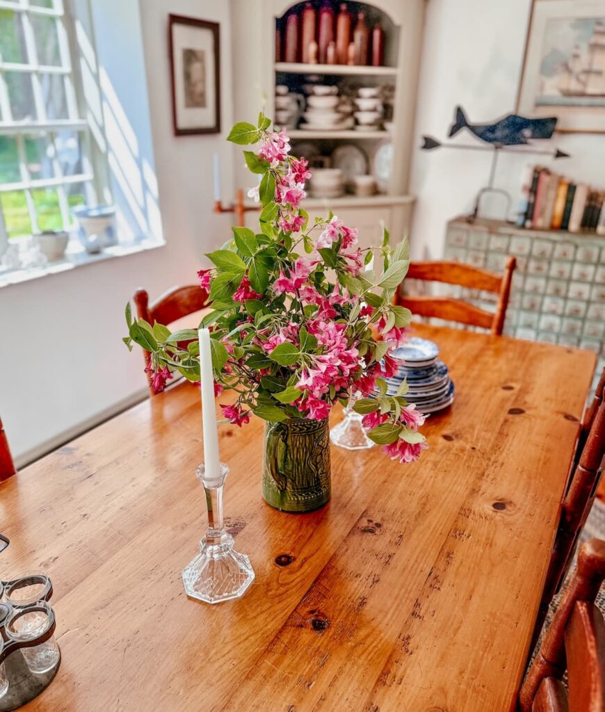Vintage pine wooden rectangular table vs. round table with pink and green centerpiece in long narrow dining room.