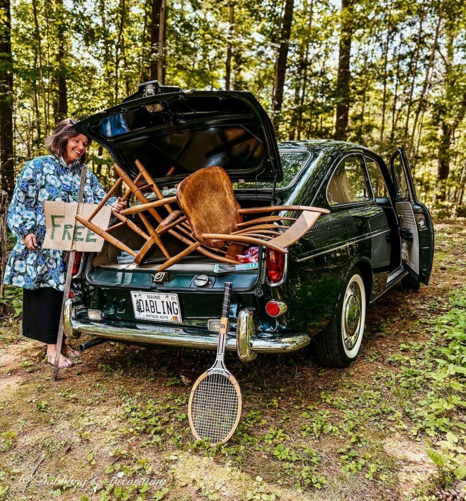 Ann vintage home decor blogger looking into back of vintage VW car on a thrift store road trip with wooden chairs, tennis racket and Free sign.