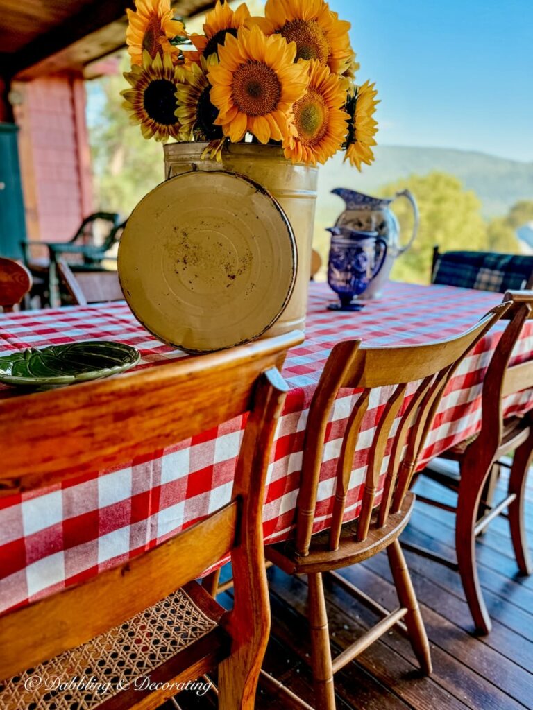 Red gingham table cloth on outdoor porch table with wooden chairs and vintage inspired sunflower centerpiece on fall table decor.