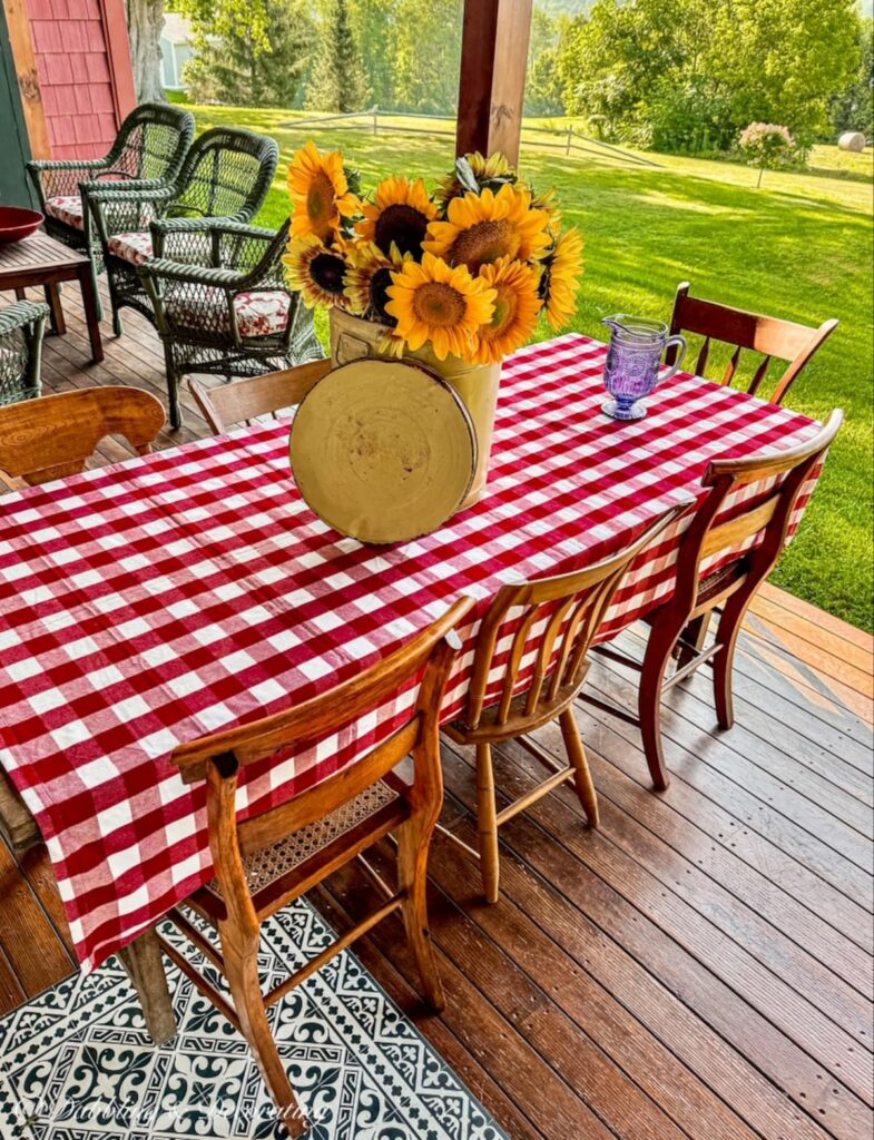 Outdoor porch table with red gingham table cloth in fall table decor. And Yellow tub filled with sunflowers.