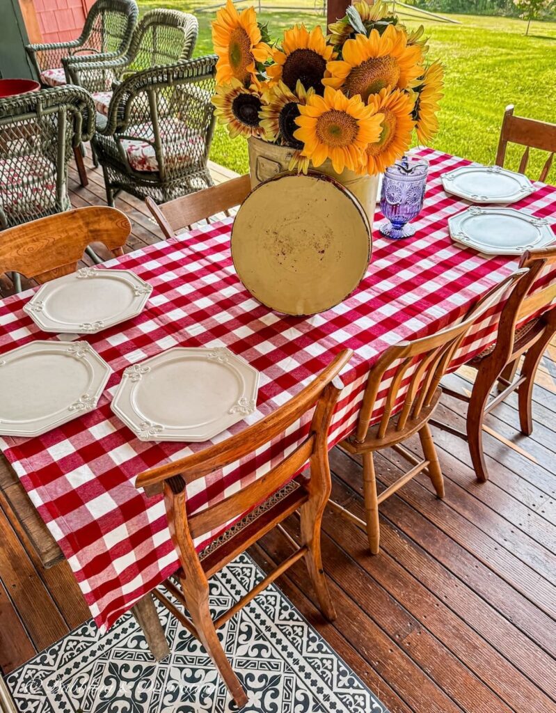 Fall Table decor with red gingham tablecloth, thrifted white chargers from Goodwill and a sunflower centerpiece on outdoor porch in Vermont.