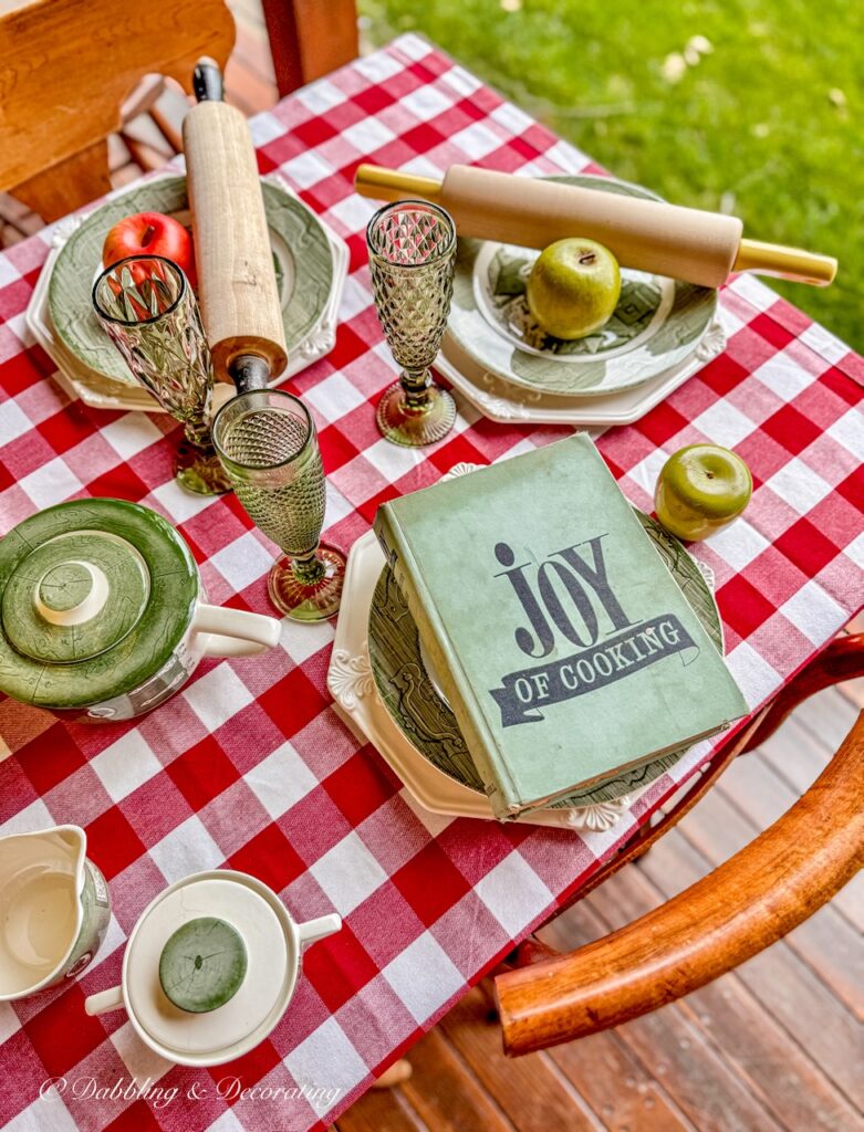 Cozy fall table decor ideas with red gingham and green and white thrifted dishes on outdoor porch.