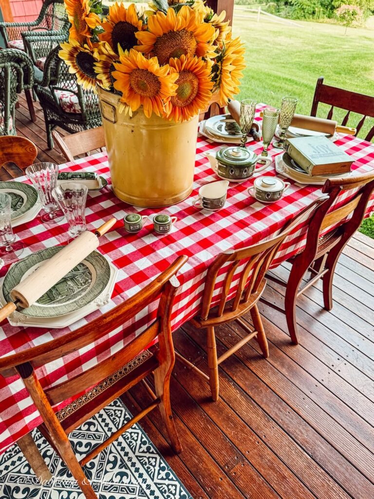 Fall tablewares with red gingham tablecloth, yellow bucket of sunflowers and Royal Colonial thrifted dishes on outdoor porch.
