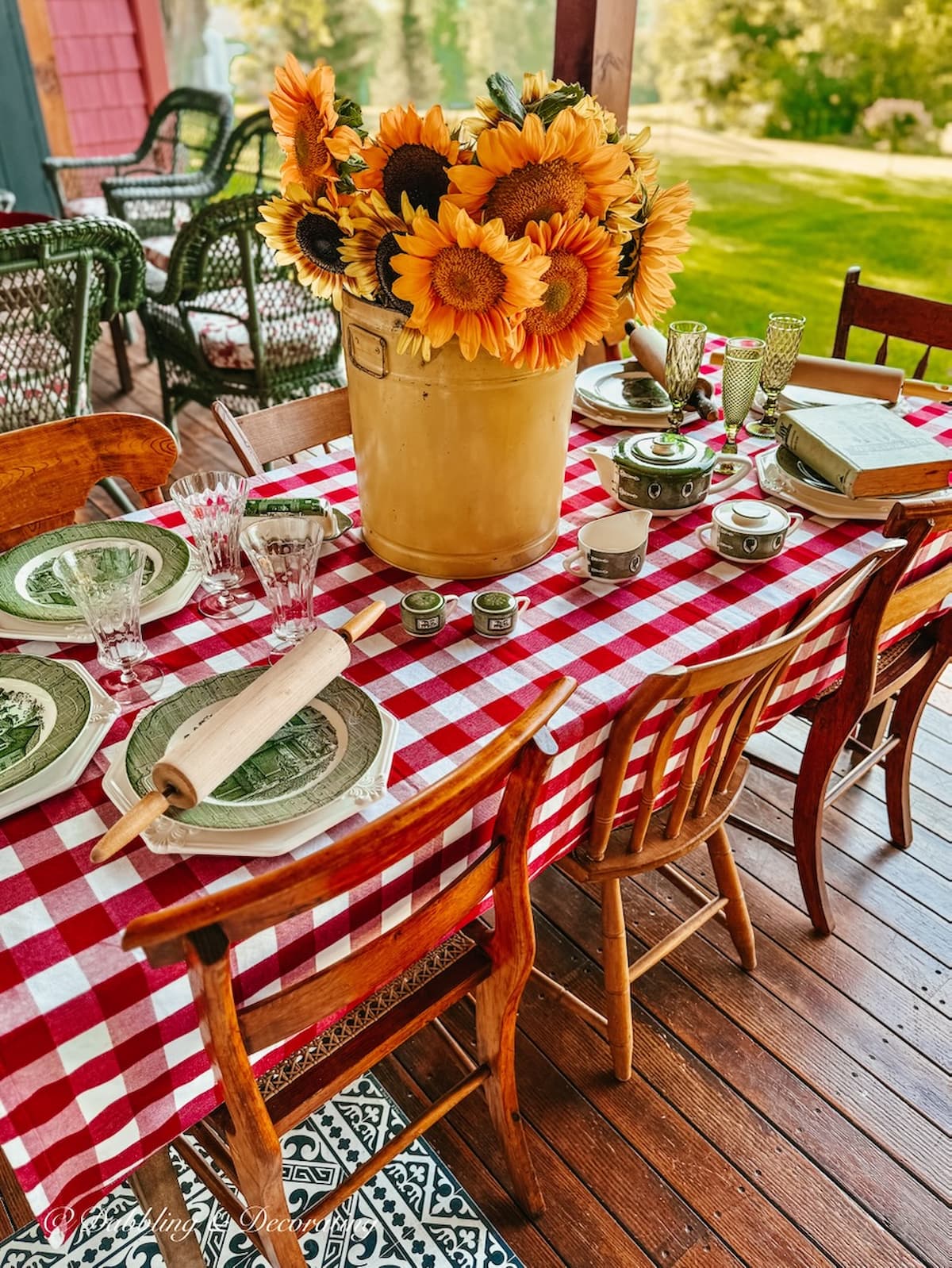 Outdoor porch table decorated with red gingham tablecloth, vintage yellow tin of sunflowers and Royal Colonial thrifted dinner place settings. Fall Decor Table Staples. Eclectic Decorating Style on Porch.