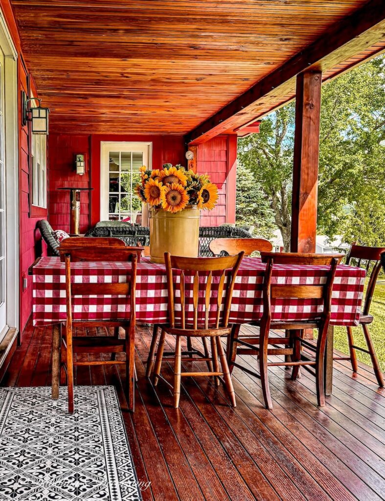 Eclectic Decorating Style on covered porch with gingham red on table with collected vintage wooden chairs and a centerpiece with a yellow tin and sunflowers.