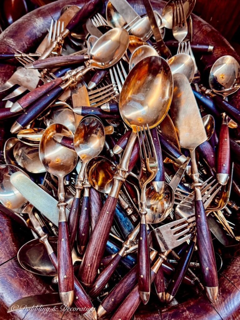 Vintage bowl of flatware in gold and wooden handles displayed in antique store.