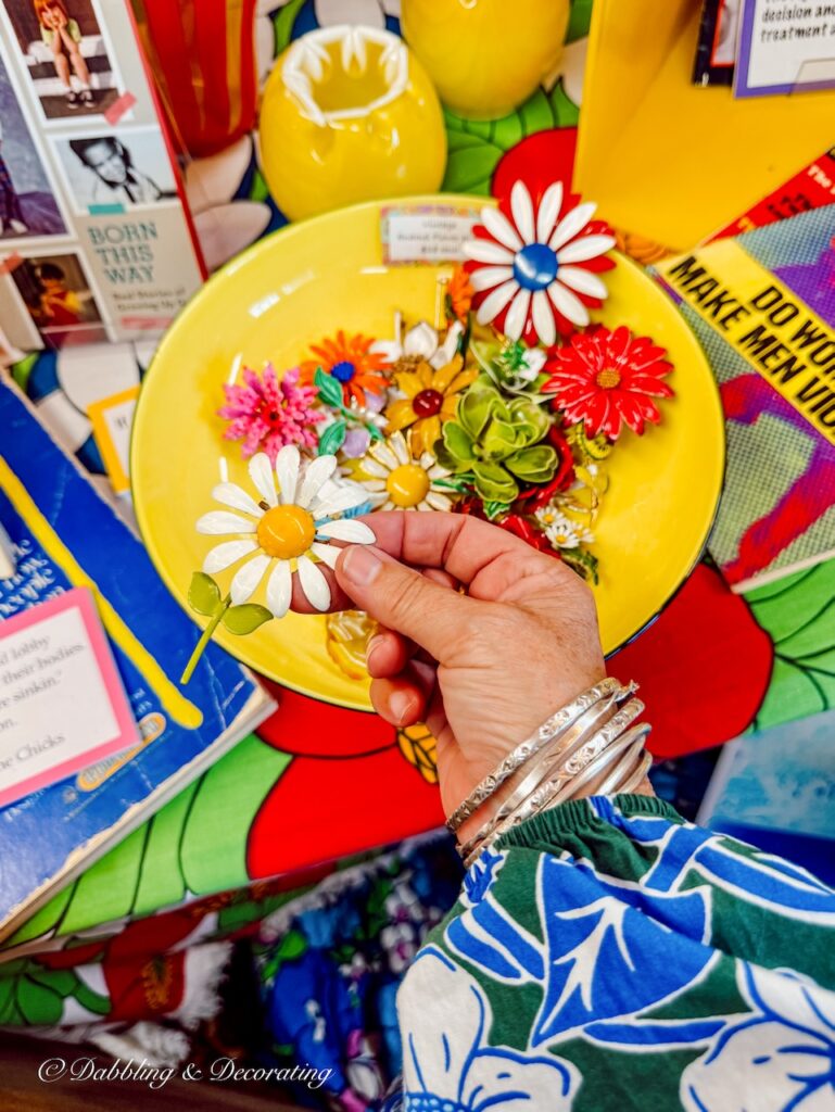 Yellow bowl of vintage pins and a retro daisy pin in hand on New Hampshire's Antique Trail.