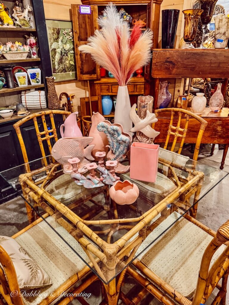 Pink and deco decor in antique store display on bamboo glass table and chairs.