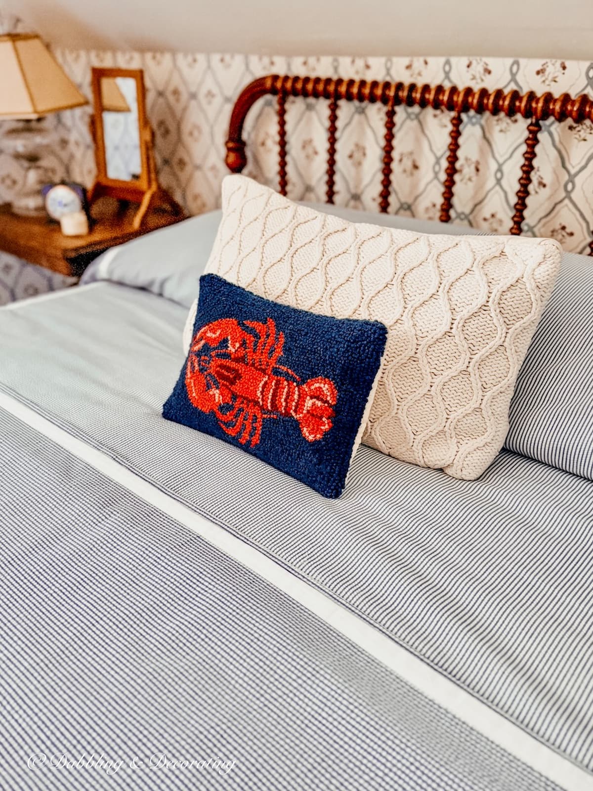 Lobster Pillow and sweater pillow on seersucker bedding on antique wooden spindle bed in small guest bedroom. Vintage Americana decor styling for summer.