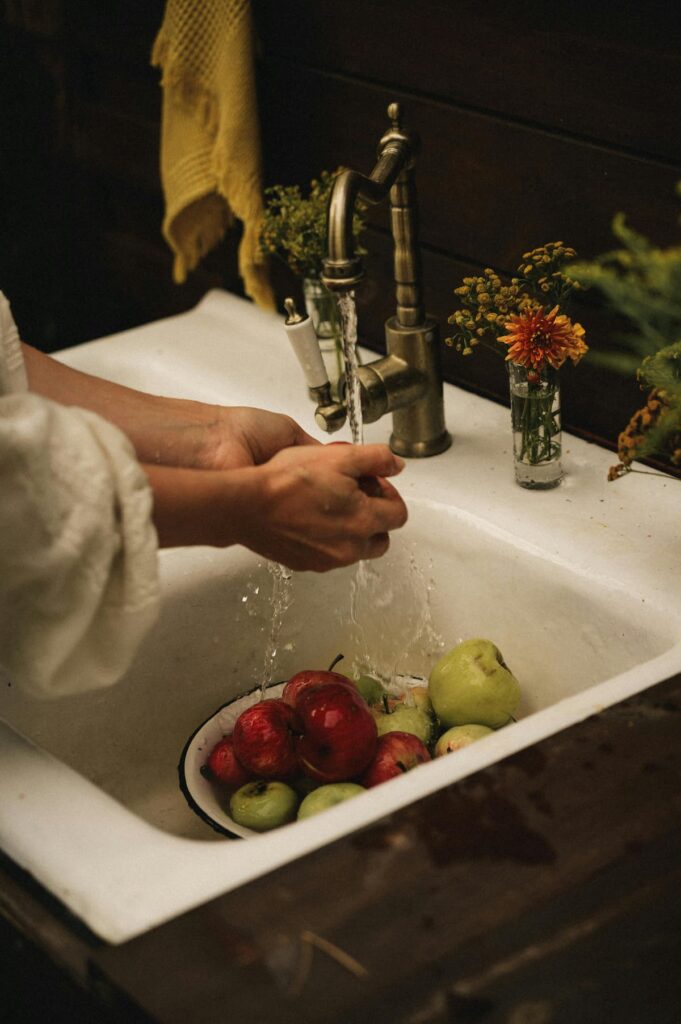 New England Farmhouse sink with a bowl of apples and running water with woman's hands with fall decor ideas.