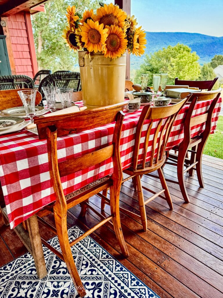 Red gingham table cloth on outdoor porch table with vintage chairs and a sunflower bouquet in fall decor.