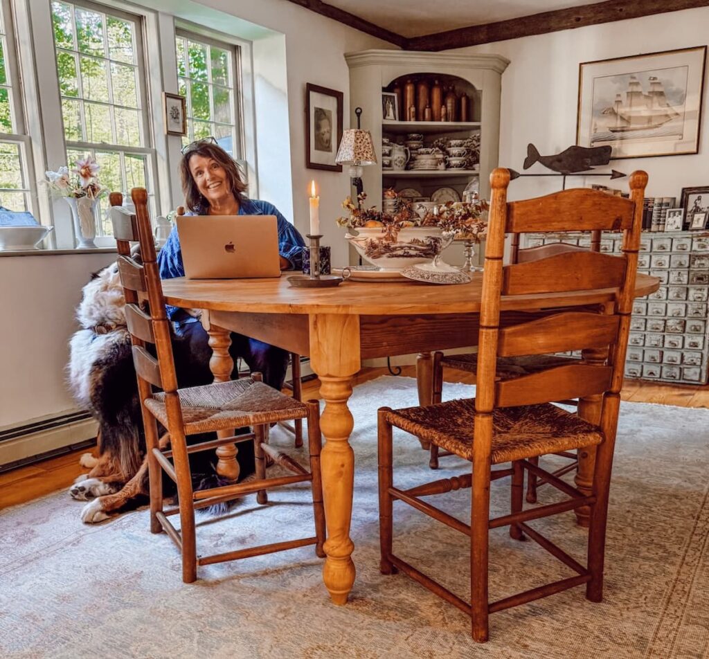 Ann, vintage home decor blogger sitting at round vs. rectangular dining table in New England home's dining room with Bernese Mountain Dog looking up.