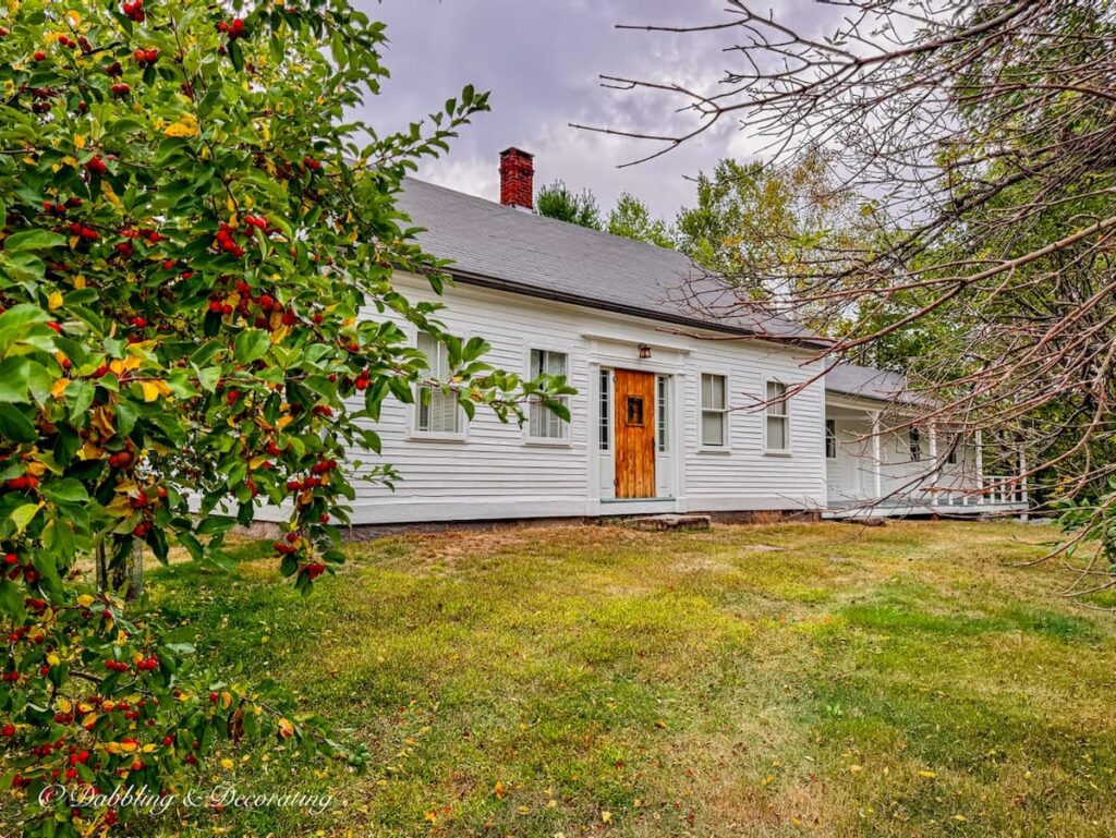 Quaint New England farmhouse white with wooden door in fall decor ideas.