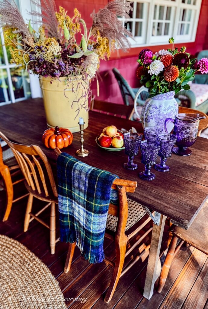 Ceramic pumpkin, blanket and purple glassware and florals gathered on outdoor vintage wooden table on porch with Goodwill Northern New England fall decor ideas finds.