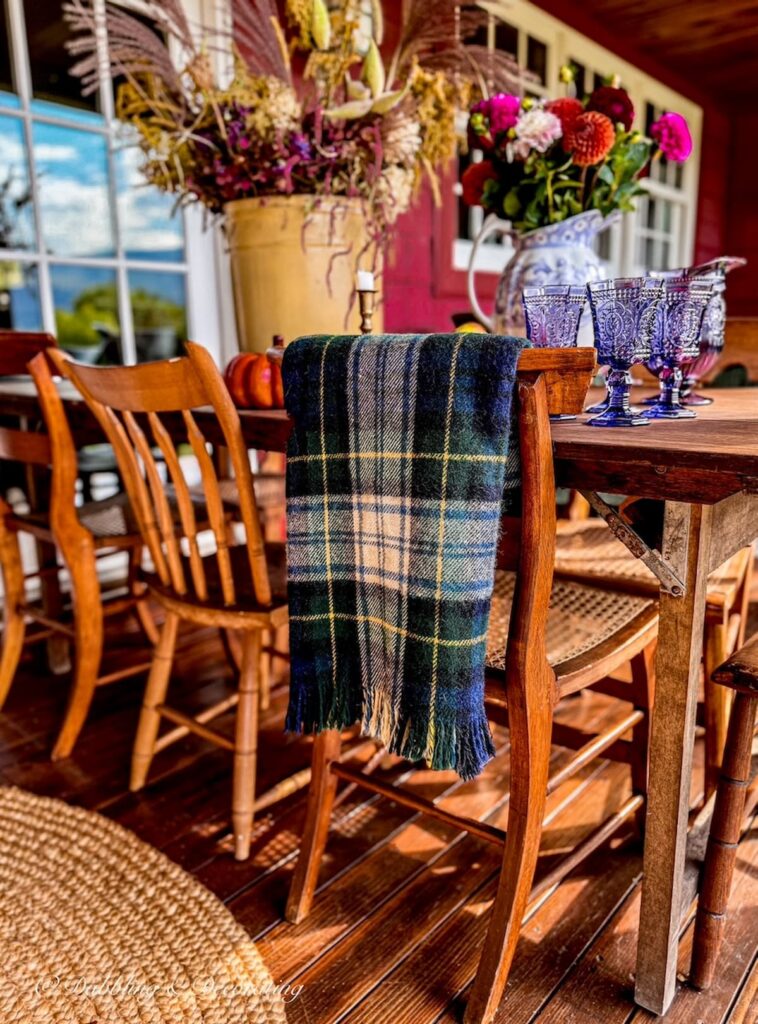 Outdoor porch vintage table with Goodwill Pendleton Blanket find hanging over thrifted wooden chair for fall decor ideas.