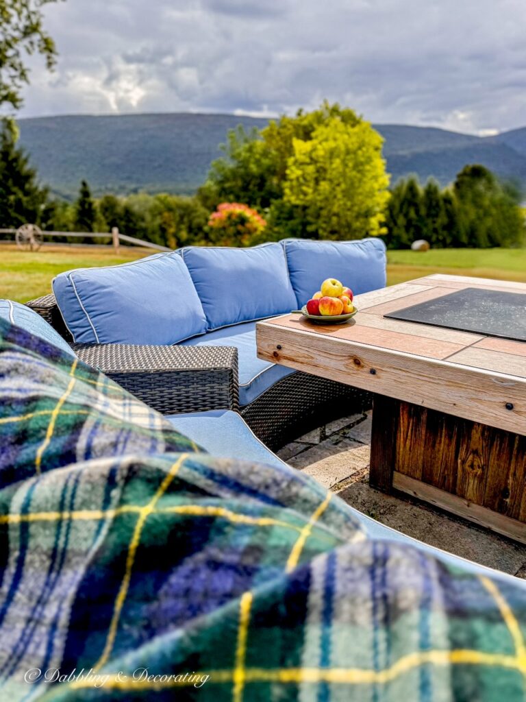 Outdoor fire pit in the mountains with Goodwill Pendleton blanket and a plate filled with apples in the Vermont mountains with blue conversational set.