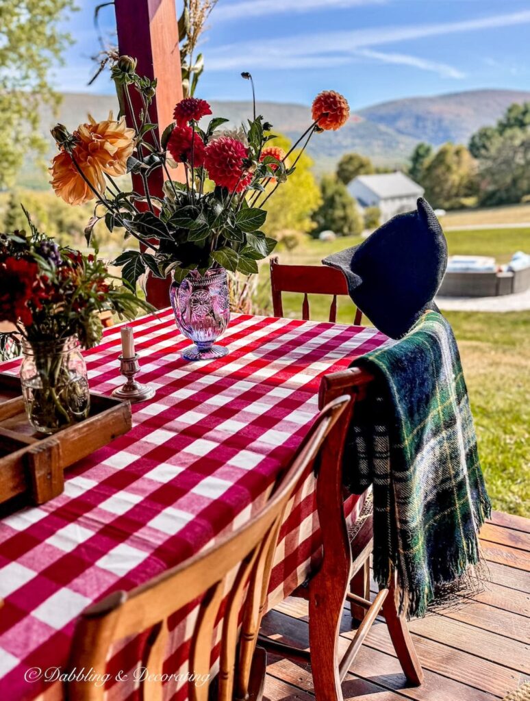 Fall decor ideas with red gingham tablecloth, vintage wooden chairs, floral arrangements and mountain views.