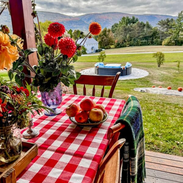 Red gingham tablecloth on outdoor porch table with brilliant fall flowers and mountain views in New England.