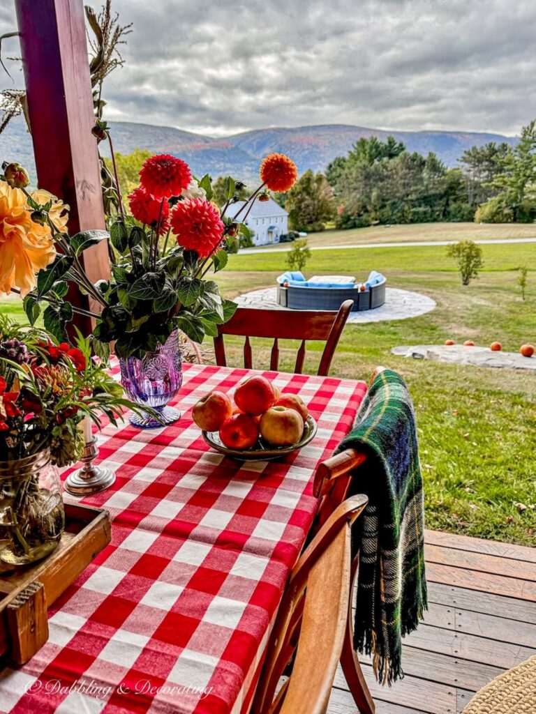 Red gingham tablecloth on outdoor porch table with brilliant fall flowers and mountain views in New England.