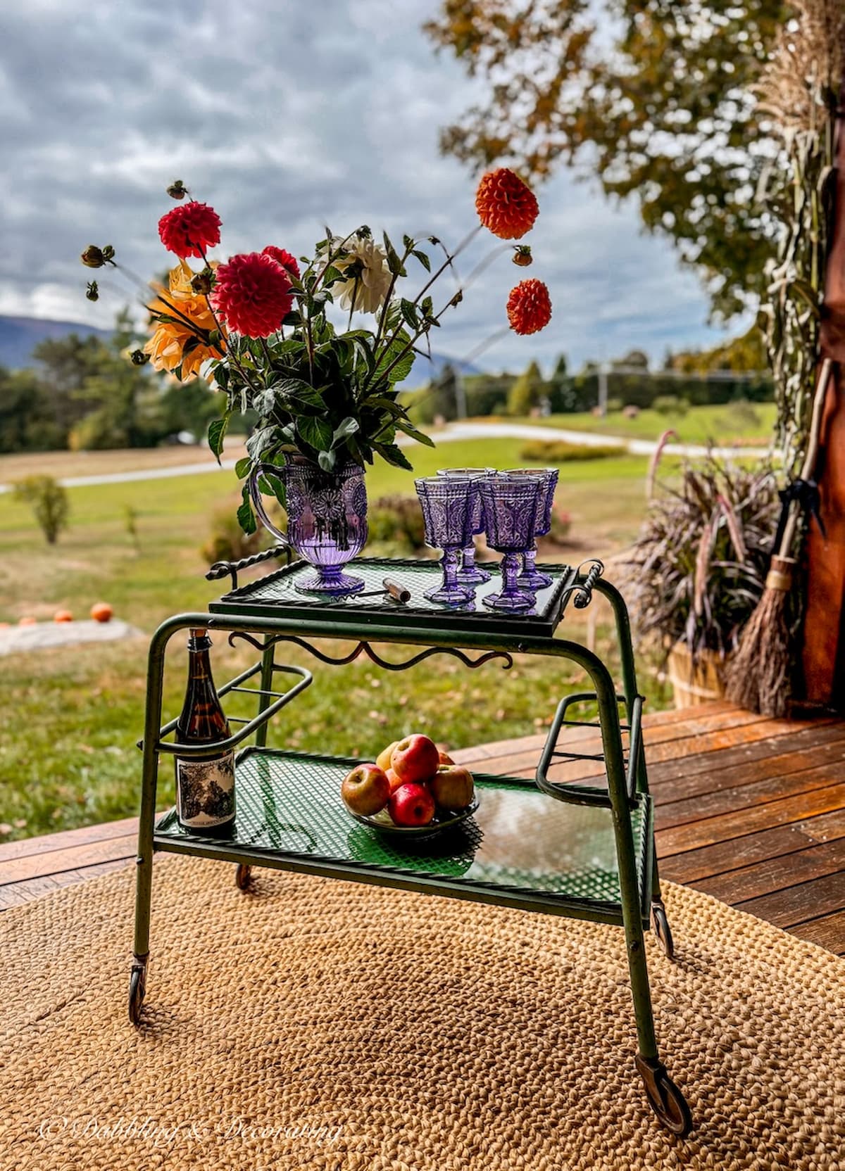 Antique beverage cart on fall porch with bouquet of fall flowers, amethyst glassware and bowl of apples with mountain views.