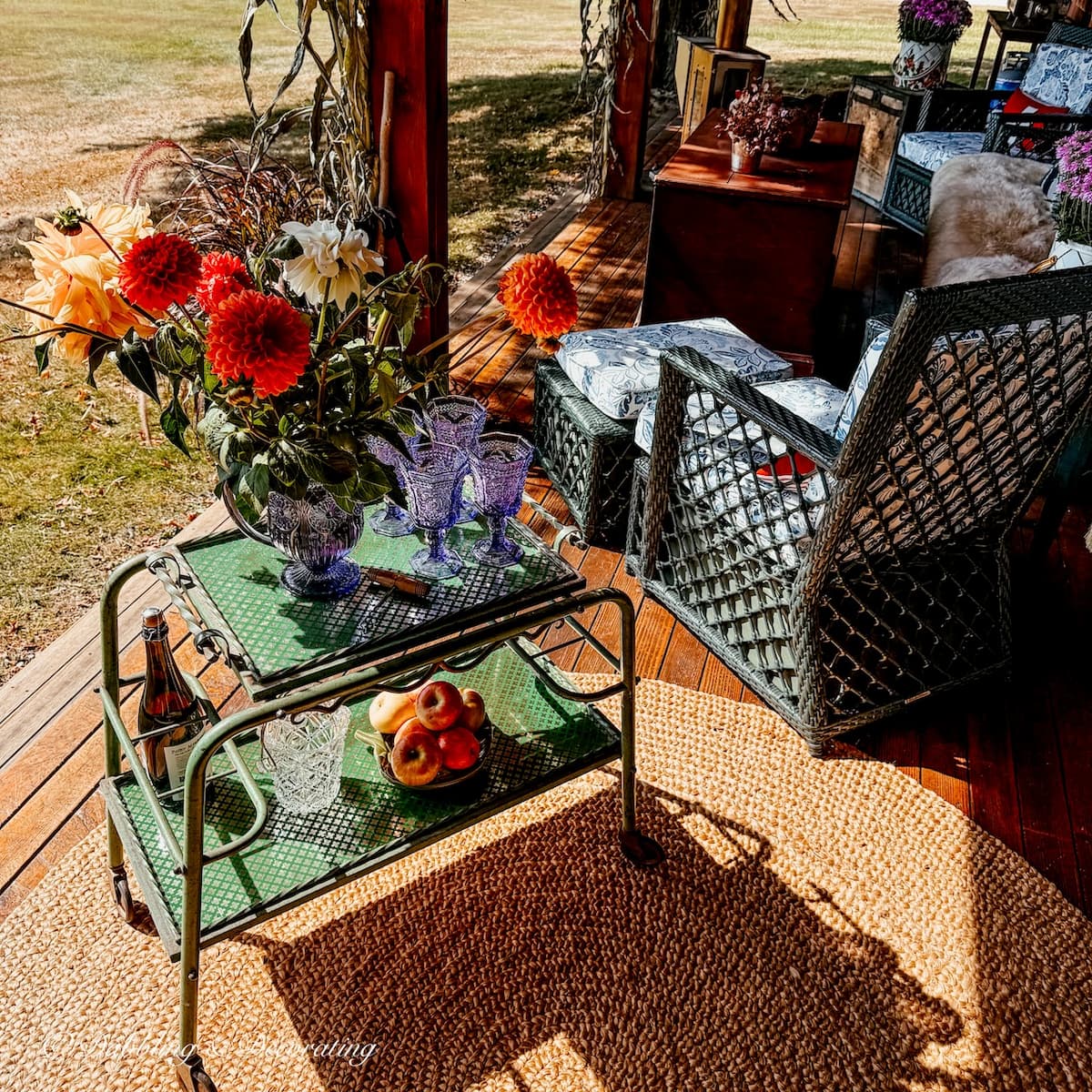 Fall porch decor with vintage bar cart, fall flowers, jute rug and cornstalks.