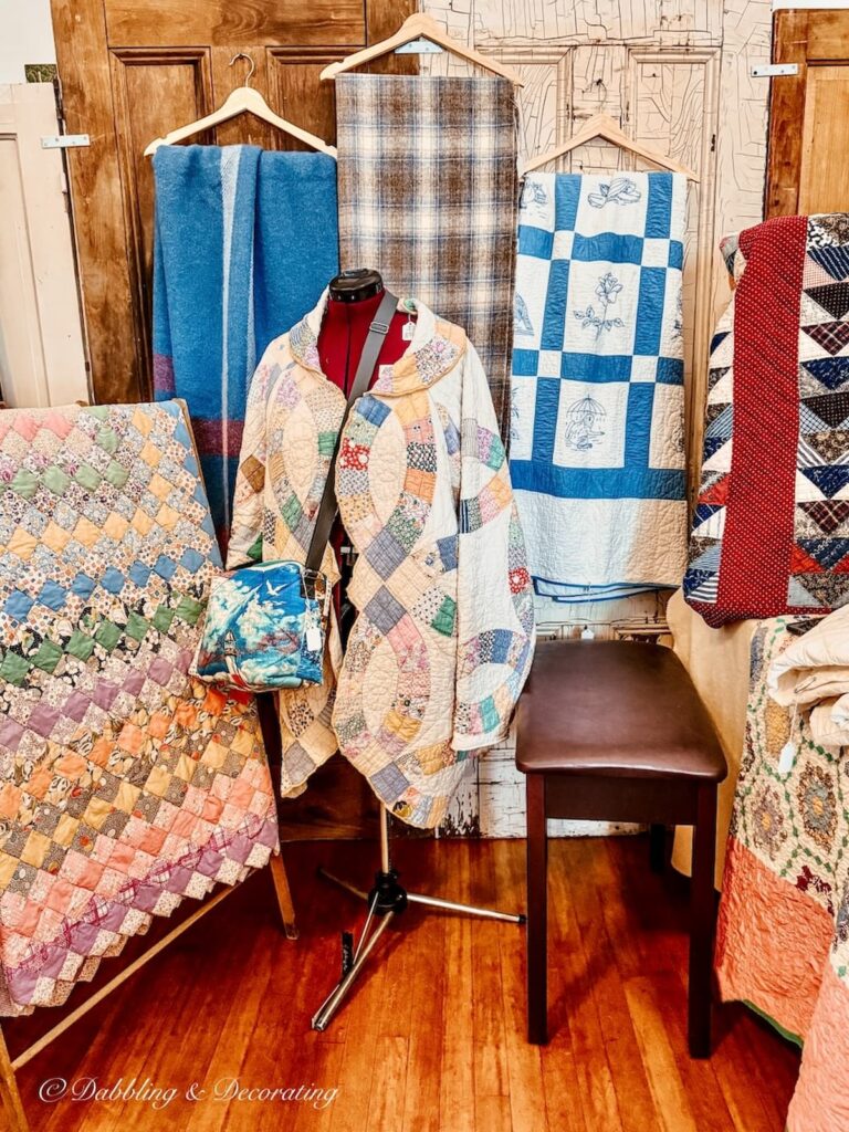 Vintage booth inside Vintage and Vogue Pop-Up Market filled with quilts and blankets and mannequin with a vintage coat.