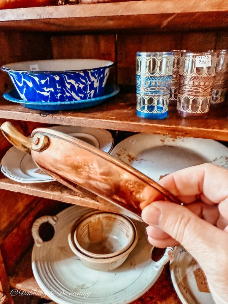 Vintage copper kitchen accessory in hand in front of cupboard at Vintage and Vogue Market.
