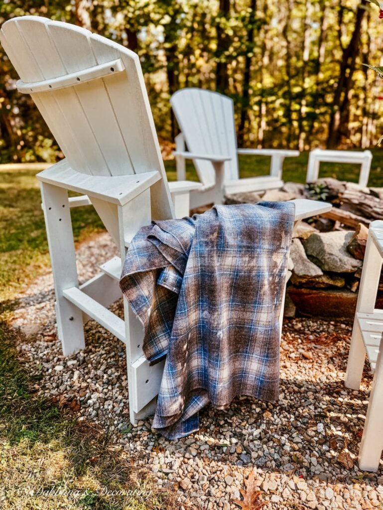 Vintage blue and brown Woolrich swatch draped over white New England Adirondack chair at a fire pit in backyard.