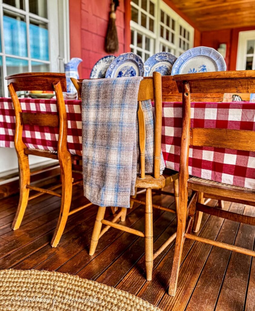 Outdoor porch table with vintage wooden chairs decorated for fall with a blue and brown vintage Woolrich swatch draped over chair from Vintage and Vogue Market.