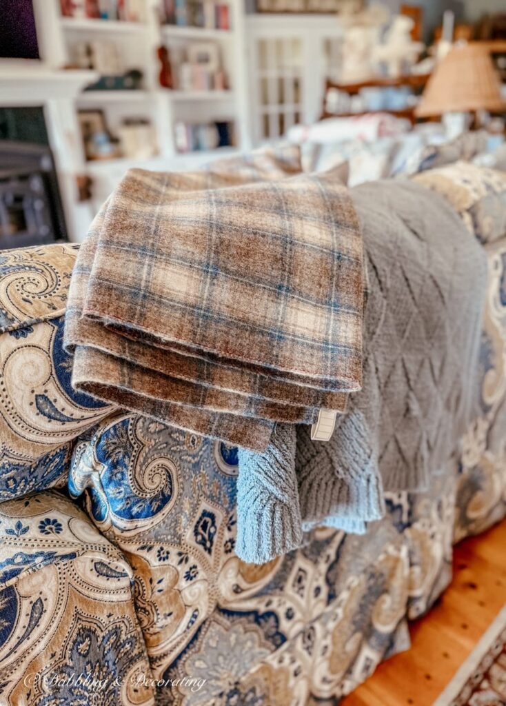 Blue and brown vintage Woolrich blanket size swatch layered over blue and brown paisley couch and blue blanket in living room.