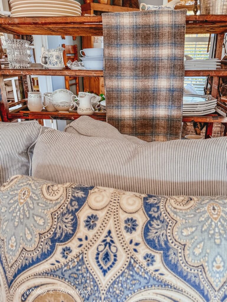 Vintage brown and blue plaid vintage Woolrich blanket-sized swatch folded and hanging on back of vintage cobbler rack in contrast with paisley and striped love seat in living room.