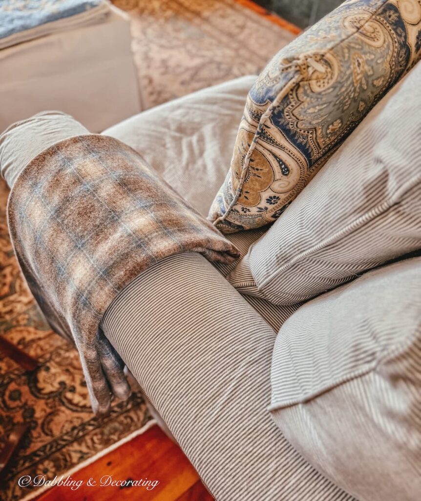 blue and brown plaid vintage Woolrich blanket size swatch folded over blue and white striped love seat armrest next to blue and brown paisley pillow in living room.