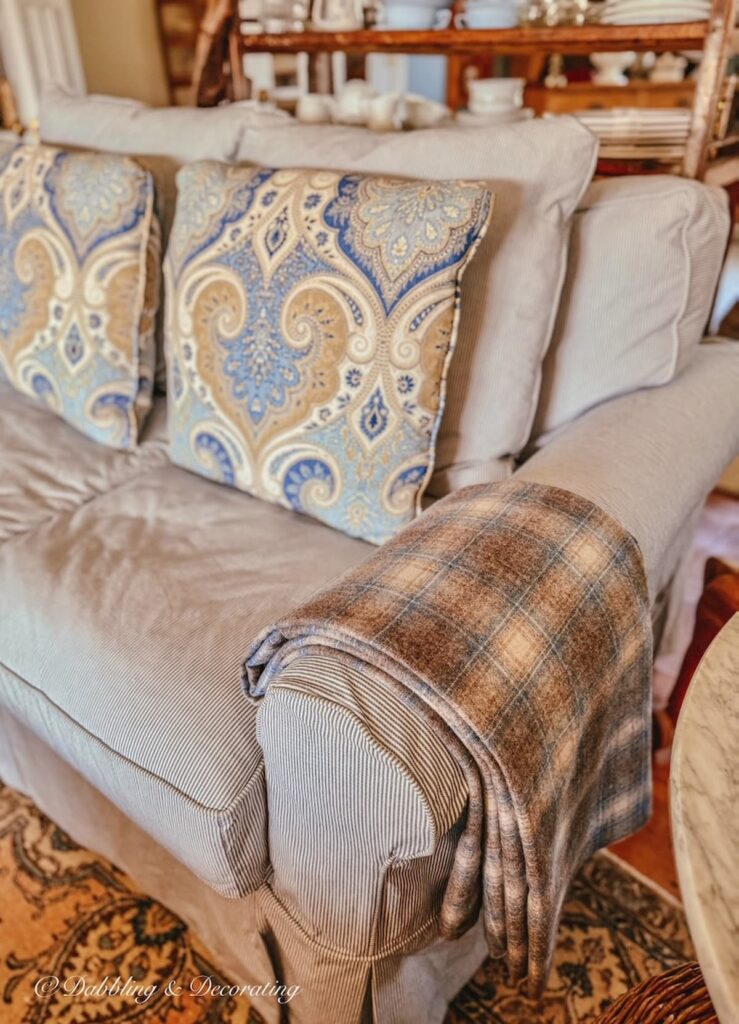 blue and brown plaid vintage Woolrich blanket size swatch folded over blue and white striped love seat armrest next to blue and brown paisley pillow in living room.