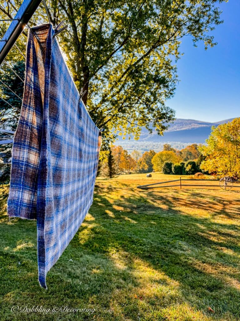 Vintage blue and brown Woolrich swatch blanket size hanging on clothesline with fall foliage mountain scenery in early morning.