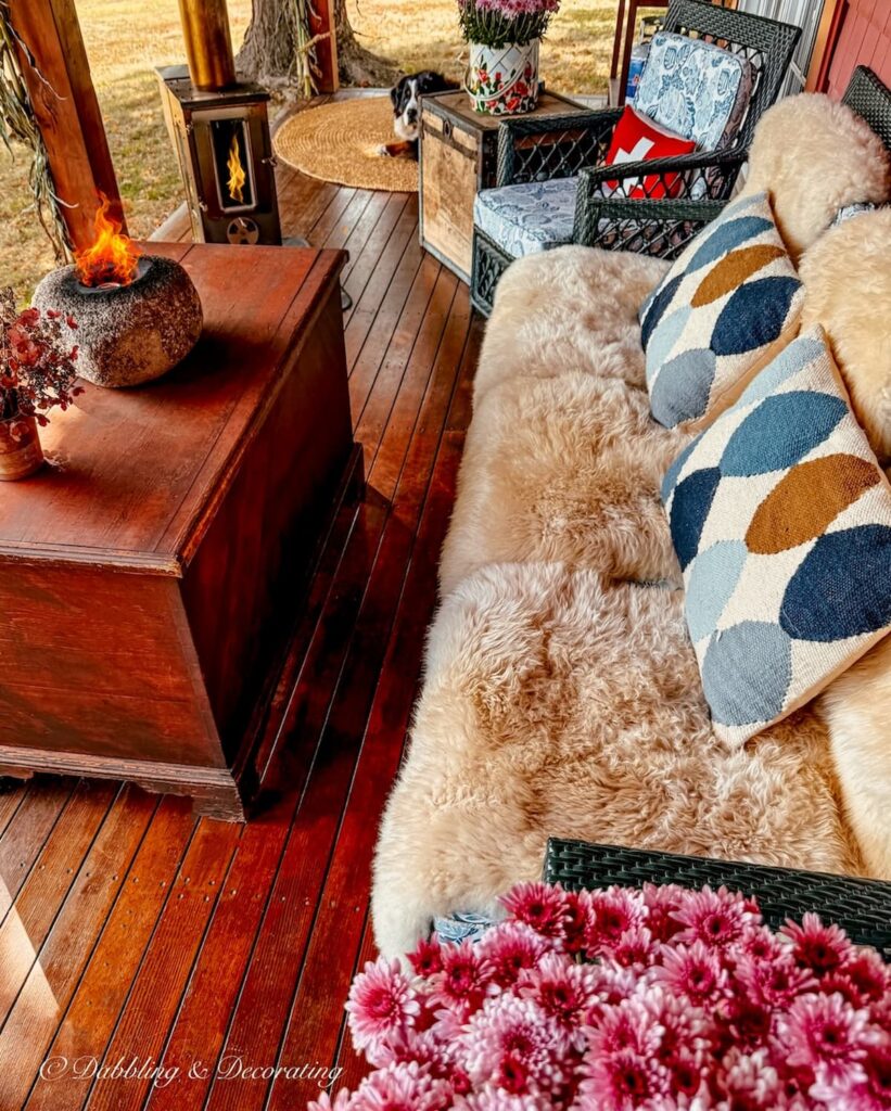 Fall porch decor ideasa with cozy sheepskins and layered blue and brown pillows on covered porch with pink asters.