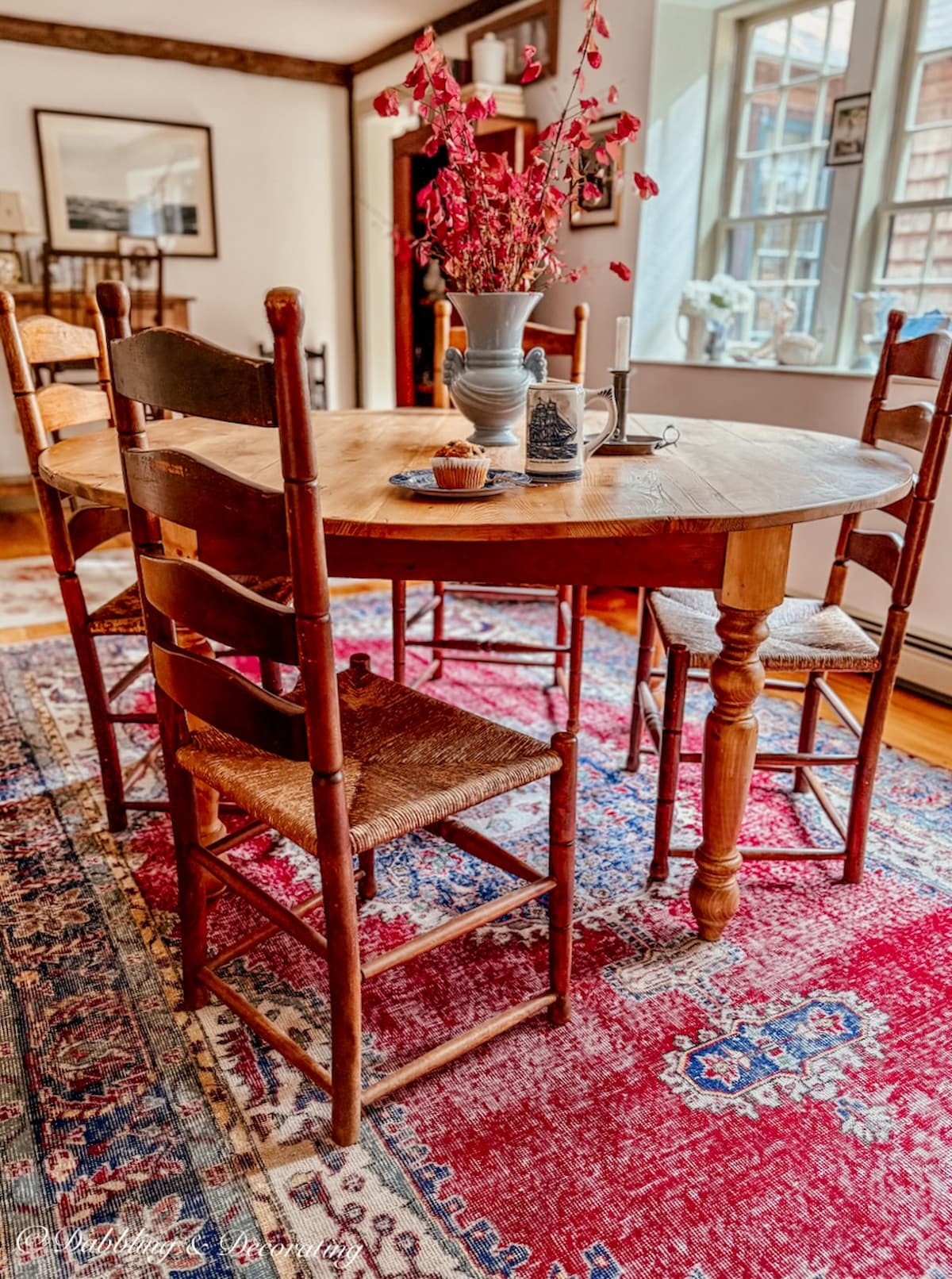 Vintage pine wood round table with four ladder back chairs and a beautiful red vintage Turkish rug in dining room.