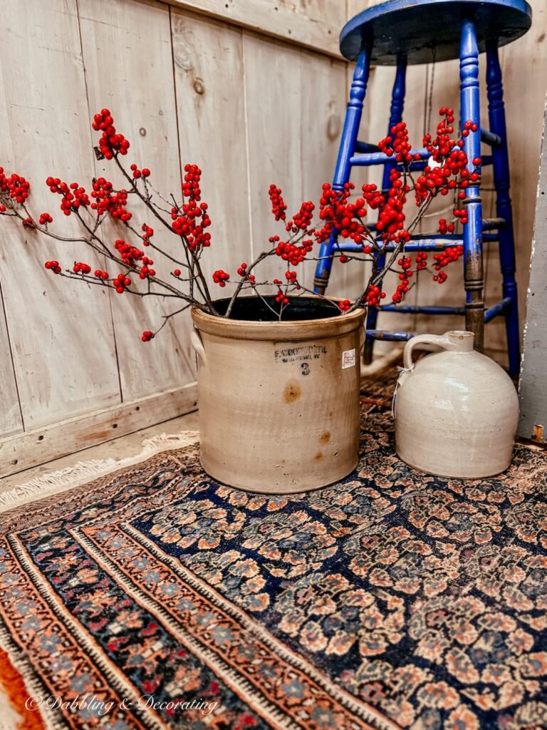 Antique crock filled with red winter berries on the floor of an antique booth.