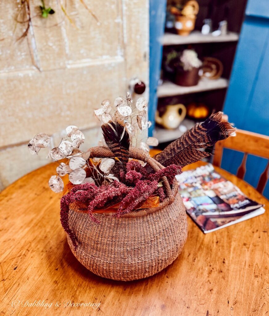Basket of feathers and purple dried flowers for Thanksgiving vintage decor on a round pine table in antique store.