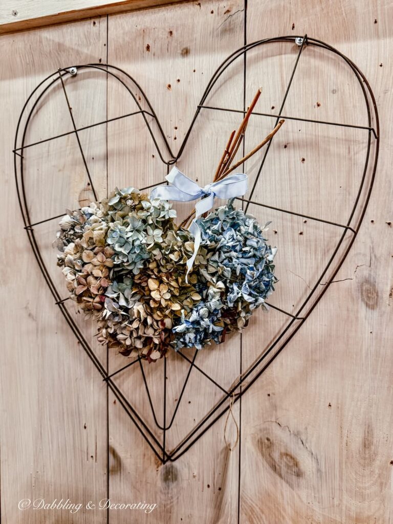 Wired vintage heart on wall with dried blue hydrangeas in antique store.