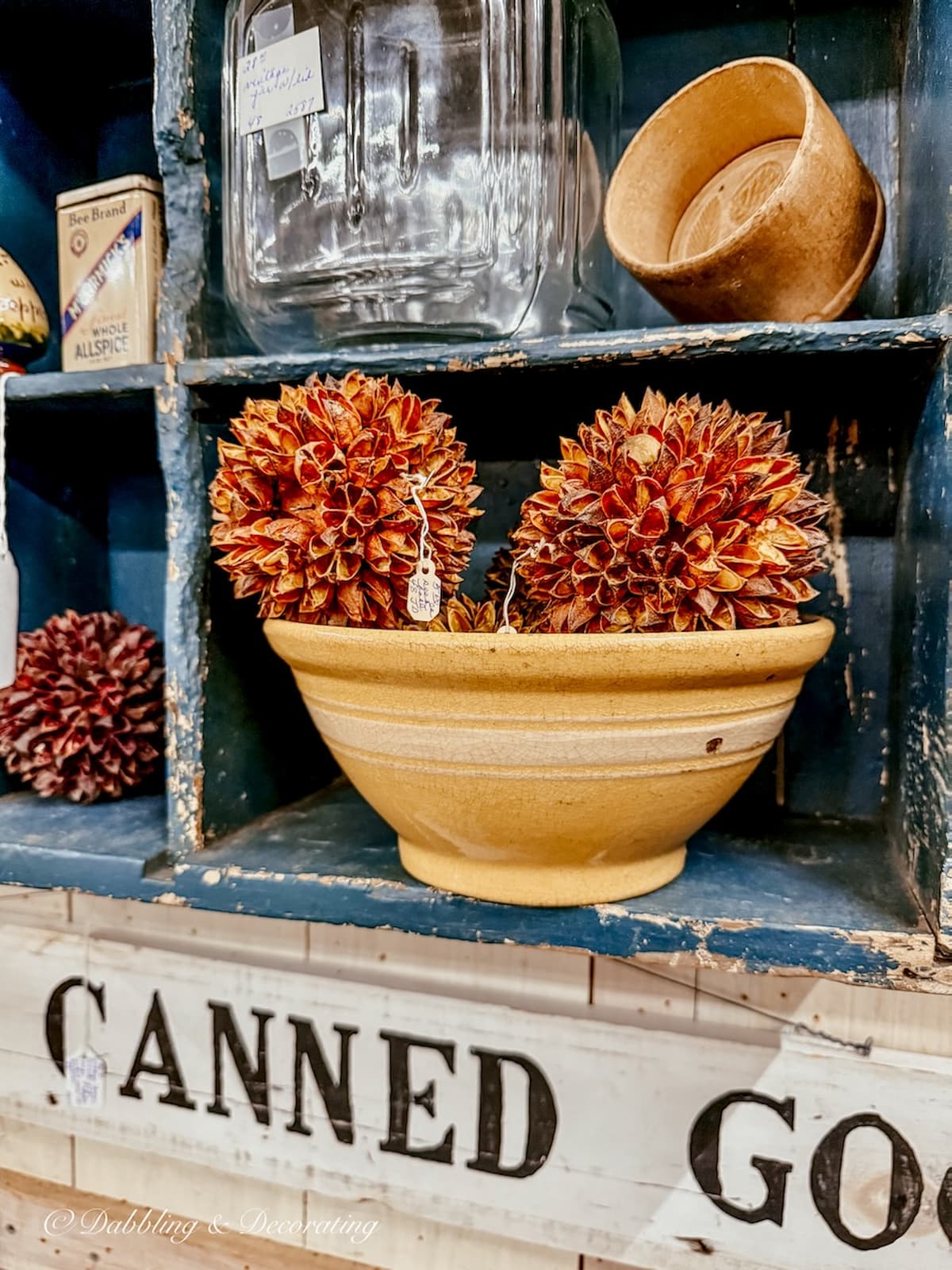 Antique yellow ware bowl on blue antique shelving with balls of textured pinecones.