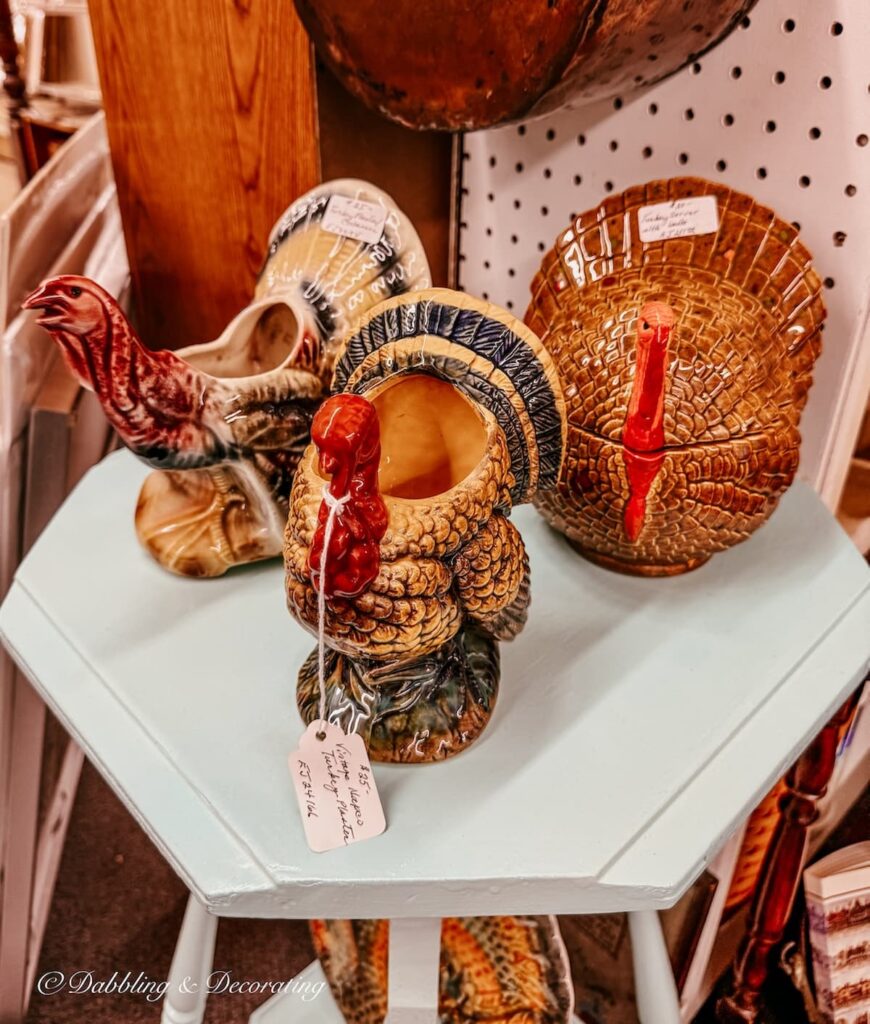 Three porcelain vintage turkey planters on a table in antique store for Thanksgiving vintage decor ideas.