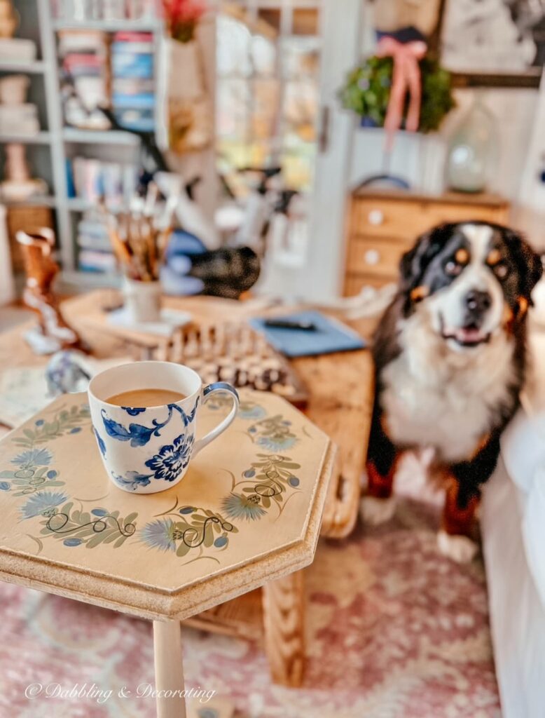 Antique side table with coffee mug and Bernese Mountain Dog looking on in home's craft room.