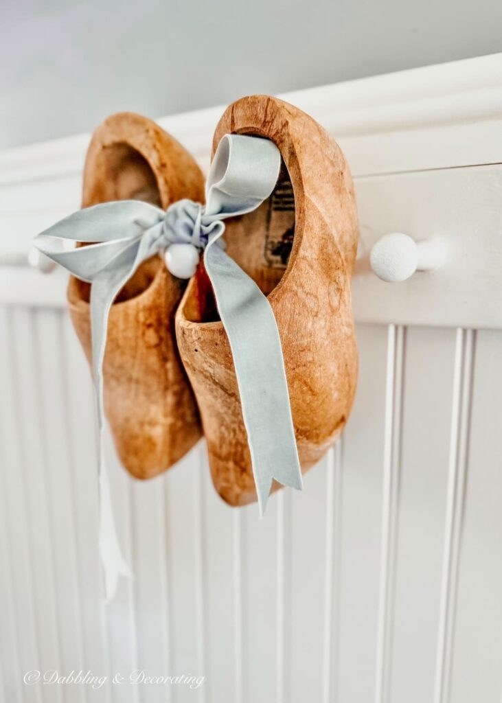 Dutch wooden clogs with soft blue bow hanging on white entryway white hooks.