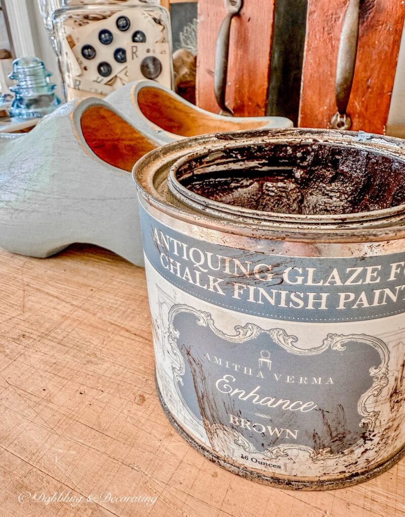 A jar of antique glaze for chalk finish paint and a pair of painted Dutch wooden clogs on table.